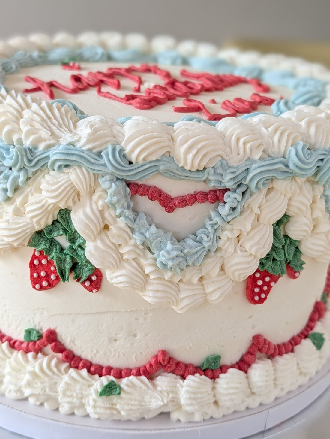 Vintage-style birthday cake with blue, red, and white buttercream piping and strawberry details from Happy Hippo Bakery in Hutto, Texas